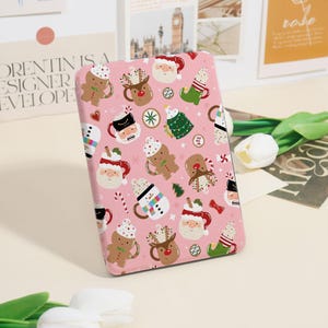 May include: A pink rectangular case featuring a repeating pattern of Christmas-themed illustrations. The design includes gingerbread men, Santa Claus, reindeer, mugs, Christmas trees, and candy canes. The case is likely for a phone or tablet.