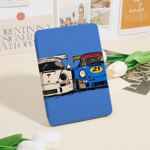 Peut inclure: Une coque de tablette bleue avec un graphisme de deux voitures de course classiques, une blanche et une bleue. La voiture blanche porte un "T" noir à l'avant, et la voiture bleue porte le numéro "21" sur un cercle jaune. La coque a une finition brillante.