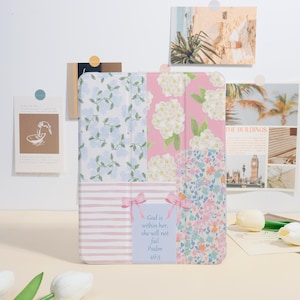 Peut inclure: Une housse de tablette à motifs multiples avec des motifs floraux et rayés aux couleurs pastel. L'étui comprend une section rose avec des fleurs d'hortensia blanches et une section avec le texte "God is within her, she will not fail Psalm 46:5".