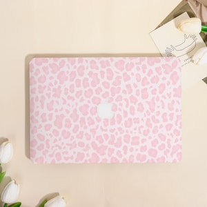 May include: A pink and white leopard print laptop case with the Apple logo in the center. The case is rectangular and covers the top of the laptop. The design is a repeating pattern of irregular shapes.