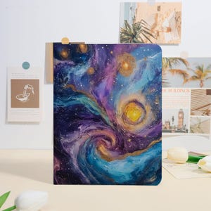 May include: A notebook with a vibrant, abstract painting of a galaxy. The artwork features swirling blues, purples, and gold accents, with a bright yellow center. The notebook is rectangular and appears to be closed.