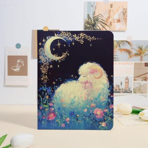 Peut inclure: Un carnet avec une illustration fantaisiste d'un mouton se reposant dans un champ de fleurs sous un croissant de lune et des étoiles. La couverture a un fond bleu foncé avec des accents dorés. Un cadeau parfait pour les amoureux de l'art et de la nature.