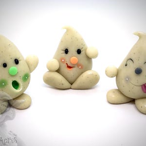 Puede incluir: Tres pequeñas figuritas blancas con forma de fantasma con diferentes expresiones faciales. El fantasma de la izquierda tiene ojos verdes y una expresión de sorpresa, el fantasma del medio tiene mejillas naranjas y una expresión feliz, y el fantasma de la derecha tiene una nariz gris y la lengua fuera.