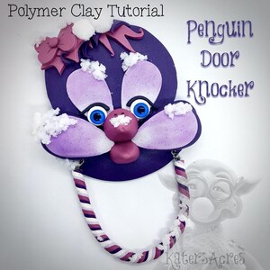 May include: Purple and white penguin door knocker with a pink bow and snow details. The knocker is attached to a white and pink striped rope.