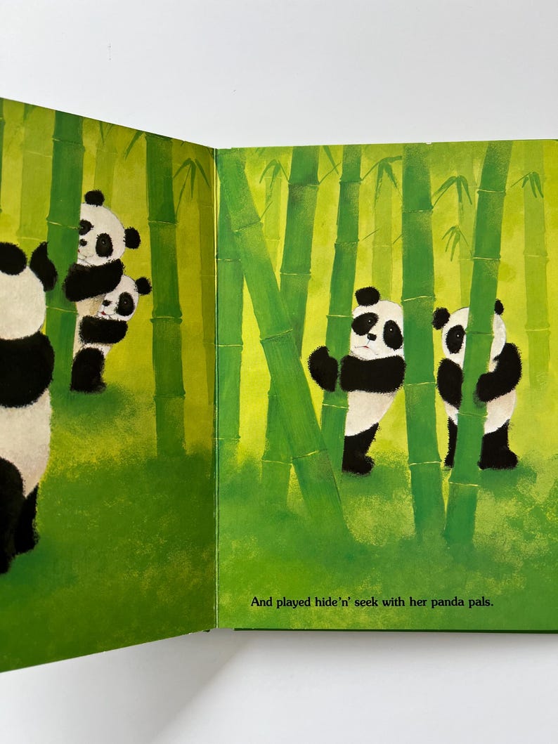 May include: An illustrated children's book spread showing panda bears in a bamboo forest. The pandas are black and white, and the bamboo is green. The text reads, "And played hide 'n' seek with her panda pals."