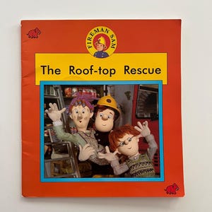 May include: A Fireman Sam book titled The Roof-top Rescue with a bright orange cover. The front features a circular logo of a firefighter and a central image of three characters, including a firefighter in a yellow helmet and two others.