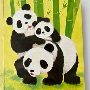 May include: A colourful children's book illustration of three pandas. The pandas are depicted in black and white with red details, set against a green background with bamboo. The text reads, "She lived with her mother and father in a bamboo forest."