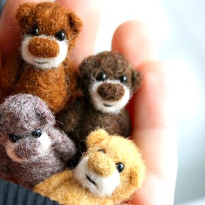 May include: Four miniature felted teddy bears in shades of brown and tan are held in a hand. The bears have small black eyes and white muzzles. The bears are a handmade craft item.