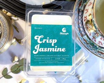 May include: A clear plastic package containing a wax melt bar. The label reads "Crisp Jasmine" with teal accents and floral designs. The wax melt is hand-poured, organic soy wax, and scented. The package contains 2.4 oz or 68 g of wax.