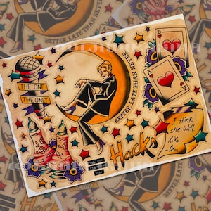 Peut inclure: Une planche de tatouage représentant une personne assise sur un croissant de lune, un micro avec une bannière THE ONE THE ONLY, deux cartes à jouer avec des cœurs, des salières et poivrières, et un parchemin avec le texte I think she Will. XoXo -Ava.