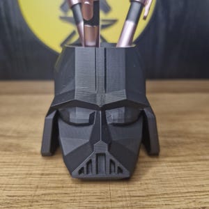 May include: A black, geometrically designed Darth Vader head is used as a pen holder. Three pens are inserted into the top of the head.