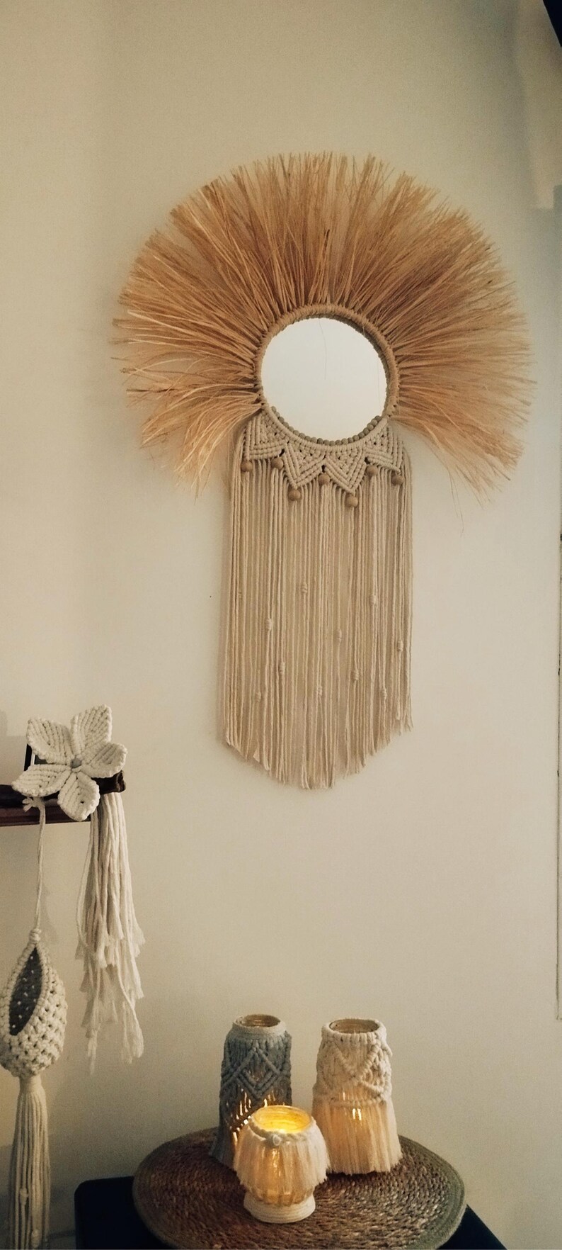 Puede incluir: Un espejo redondo con un dise&ntilde;o de sol hecho de fibras naturales. El espejo est&aacute; rodeado por un material tejido similar al rafia, con una franja de estilo macram&eacute; colgando debajo. Decoraci&oacute;n de pared de estilo bohemio.