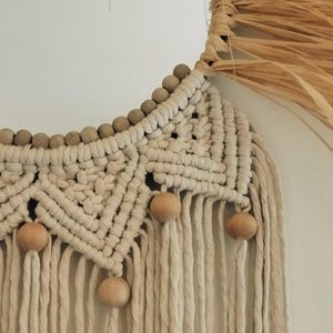 Puede incluir: Un espejo redondo con un marco de fibra natural y detalles de macram&eacute;. El marco est&aacute; hecho de un material tejido similar a la paja. El macram&eacute; presenta un patr&oacute;n geom&eacute;trico con cuentas de madera y flecos colgantes. La paleta de colores es neutra, con tonos beige y marr&oacute;n.