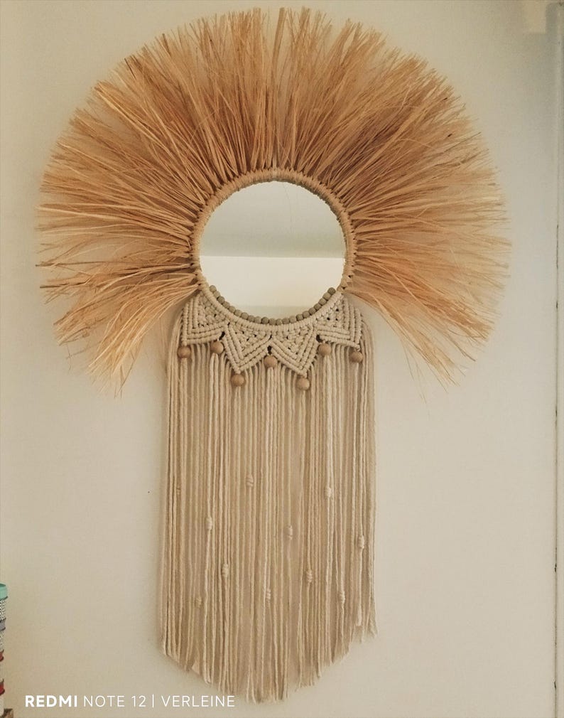 Puede incluir: Espejo de pared redondo con dise&ntilde;o de sol de fibra natural. El espejo est&aacute; rodeado por un marco de macram&eacute; beige, cuentas de madera y flecos colgantes. Una pieza decorativa para interiores bohemios o r&uacute;sticos.