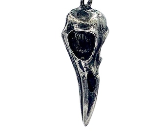 May include: A silver pendant necklace featuring a detailed bird skull design. The pendant is attached to a black cord.