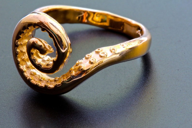 May include: A gold ring with a unique, swirling design. The ring is made of a smooth, polished metal and has a textured surface.