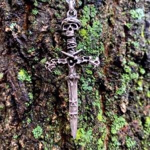 May include: A silver skull and sword pendant necklace. The pendant features a detailed skull with a wrapped sword handle and a cross-shaped hilt. The sword blade is decorated with intricate designs.