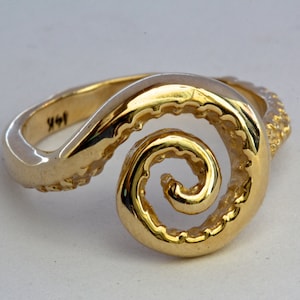 May include: A gold ring with a spiral design that resembles an octopus tentacle. The ring is textured and has a polished finish.