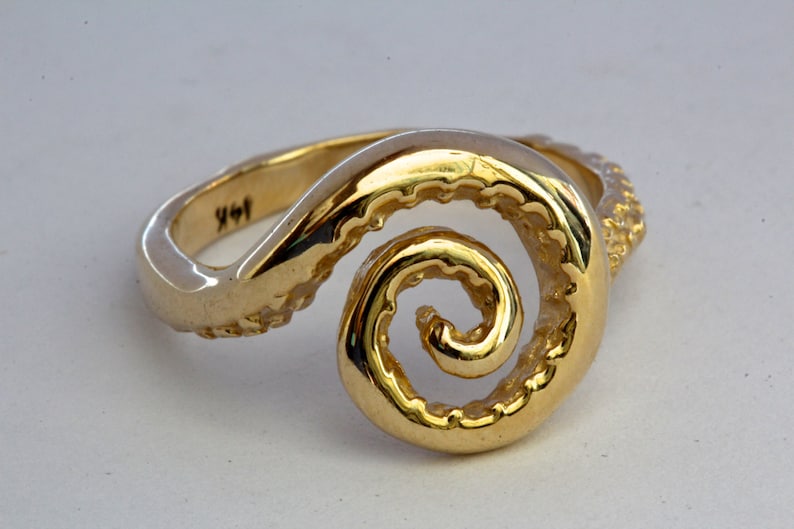 May include: A gold ring with a spiral design that resembles an octopus tentacle. The ring is textured and has a polished finish.