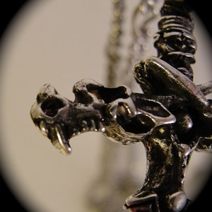 May include: Close-up of a silver dragon pendant with intricate details. The dragon's head is facing forward with its mouth open, and its wings are spread out behind it.