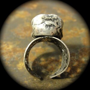 Puede incluir: Anillo plateado con un centro en forma de calavera. El anillo tiene un dise&ntilde;o abierto con intrincados patrones a lo largo de la banda. La calavera tiene una apariencia texturizada y desgastada.