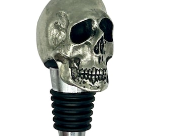 Puede incluir: Tapón de botella en forma de calavera de plata con sello de goma negro.