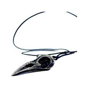 May include: A silver crow skull pendant on a black leather cord necklace.