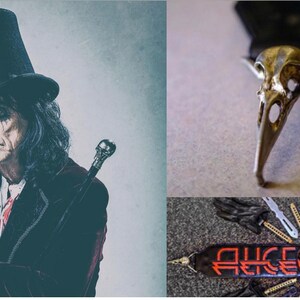 May include: A black leather guitar strap with the text "ALICE COOPER" in red and white lettering. The strap features a silver skull with a bird beak.