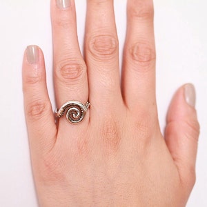 May include: A silver ring with a spiral design. The ring is on a person's finger.