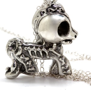 Könnte beinhalten: Eine silberne Halskette mit einem Anhänger, der eine detaillierte skelettartige Ponyfigur mit einem schädelartigen Kopf zeigt. Die Kette ist silberfarben und hat ein zartes Gliederdesign.