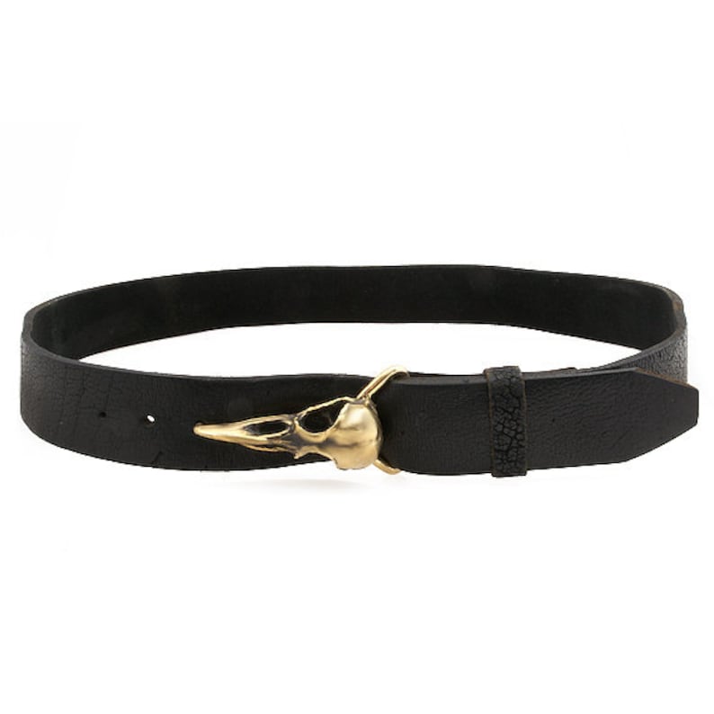May include: A black leather belt with a gold bird skull buckle.