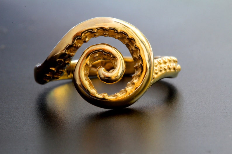 May include: A gold ring with a spiral design. The ring is made of a smooth, shiny metal and has a textured band.
