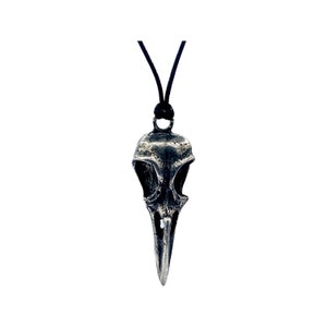 May include: A silver bird skull pendant necklace with a black cord.