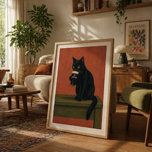 Puede incluir: Impresi&oacute;n art&iacute;stica enmarcada que presenta un gato negro sosteniendo una pinta de Guinness. El gato est&aacute; posado sobre una superficie verde contra un fondo rojo-naranja. La impresi&oacute;n est&aacute; en un marco de madera clara, agregando calidez.