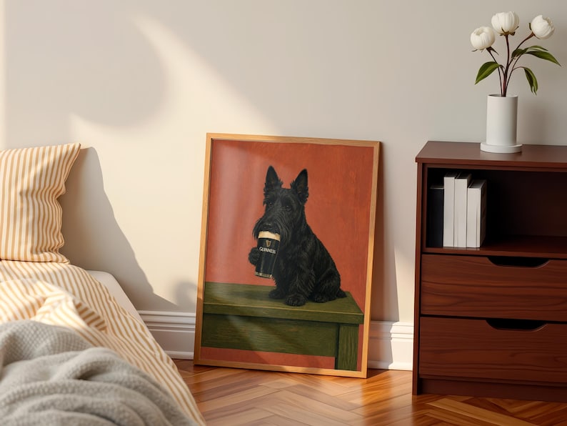 May include: A framed print featuring a black Scottish Terrier holding a pint of Guinness. The dog is sitting on a green bench against a red background. The print is in a wooden frame and is displayed in a room with a bed and a side table.