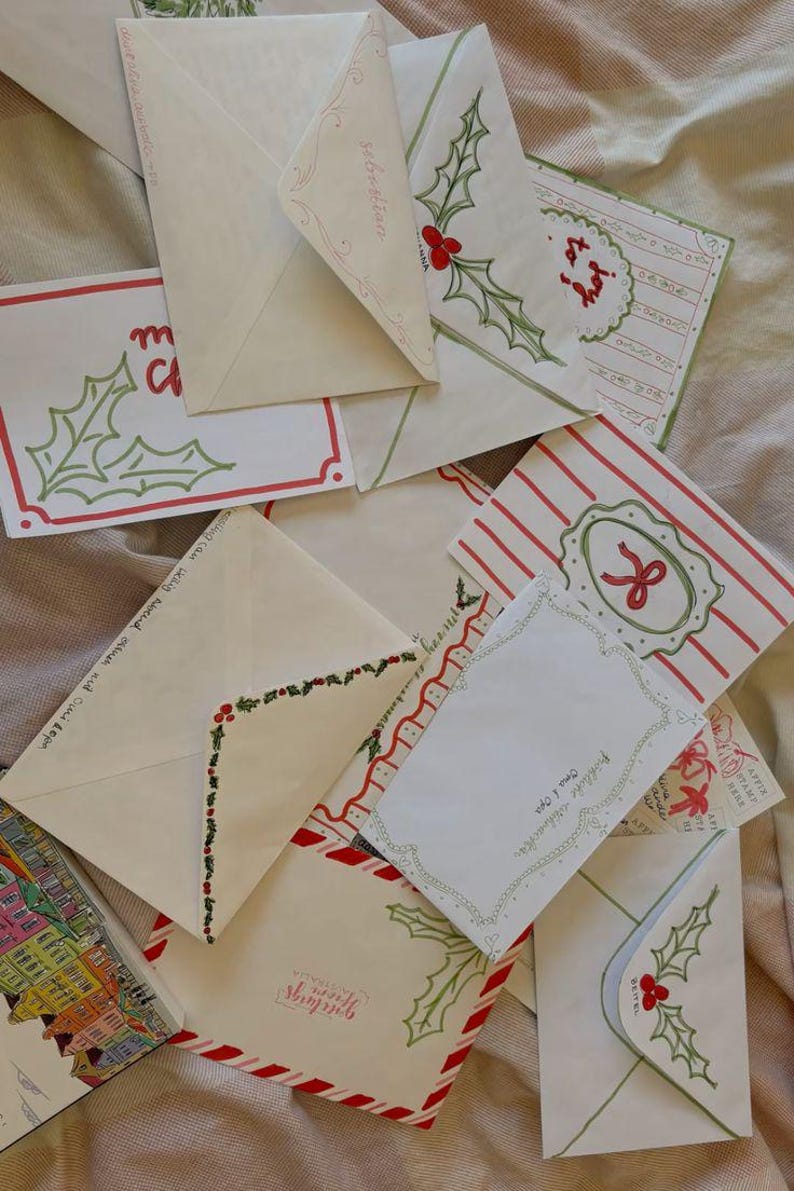 May include: A collection of Christmas-themed envelopes with various designs. Some envelopes feature holly and berry illustrations, while others have striped patterns and decorative borders. The color palette includes red, green, and white.