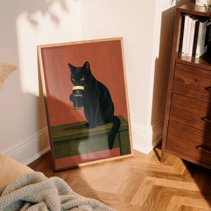 Puede incluir: Una impresi&oacute;n art&iacute;stica enmarcada que presenta un gato negro sosteniendo una pinta de Guinness. El gato, con ojos amarillos, est&aacute; sentado sobre una superficie verde contra un fondo rojo. La impresi&oacute;n est&aacute; en un marco de madera, agregando calidez a la obra.