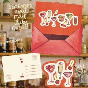 May include: A red envelope with cocktail stickers and a postcard. The stickers feature various cocktail glasses and cherries. The postcard has lines for writing and cherry illustrations. Text on the envelope reads "September snail mail club reveal!"