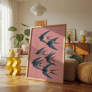 Puede incluir: Un cuadro enmarcado con una bandada de golondrinas en vuelo. Las aves est&aacute;n representadas en tonos azules, negros y rojos sobre un fondo rosa. La obra de arte se presenta en un marco de madera clara, ideal para la decoraci&oacute;n del hogar.