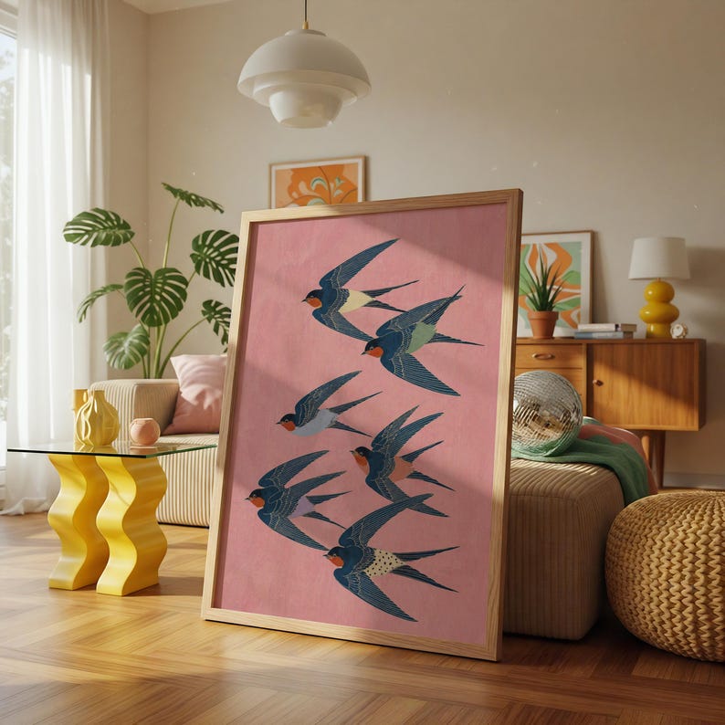 Puede incluir: Un cuadro enmarcado con una bandada de golondrinas en vuelo. Las aves est&aacute;n representadas en tonos azules, negros y rojos sobre un fondo rosa. La obra de arte se presenta en un marco de madera clara, ideal para la decoraci&oacute;n del hogar.