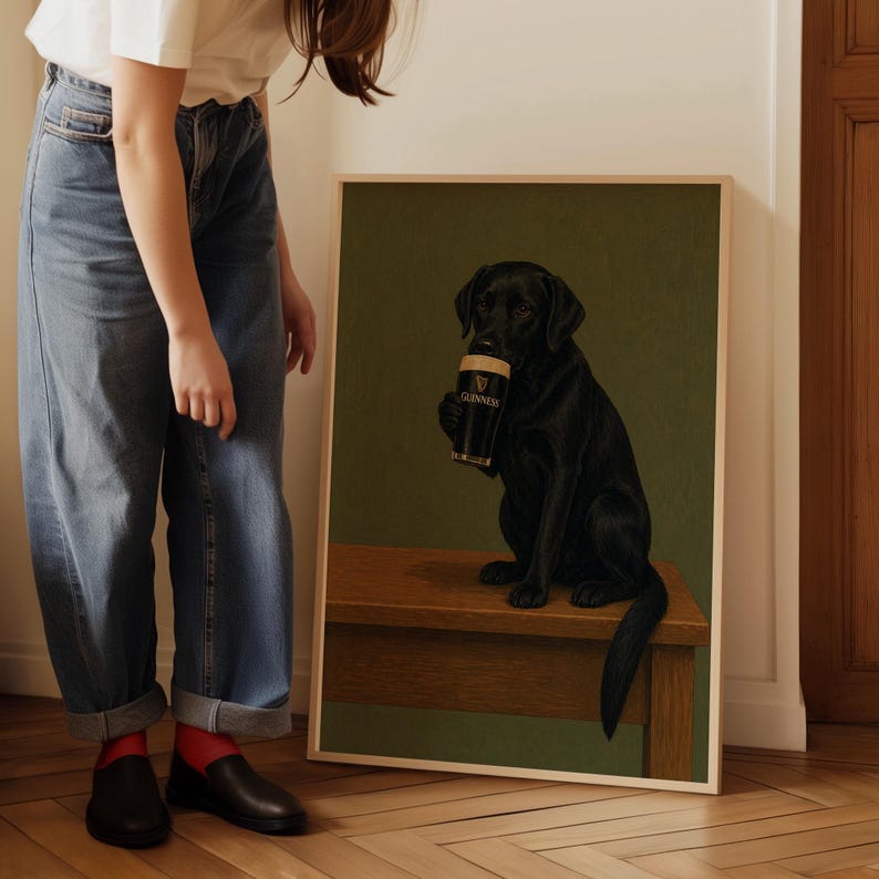 Pu&ograve; includere: Stampa incorniciata raffigurante un Labrador Retriever nero che tiene in mano una pinta di Guinness. Il cane &egrave; seduto su una superficie di legno contro uno sfondo verde. Il bicchiere di Guinness &egrave; nero con scritte bianche.