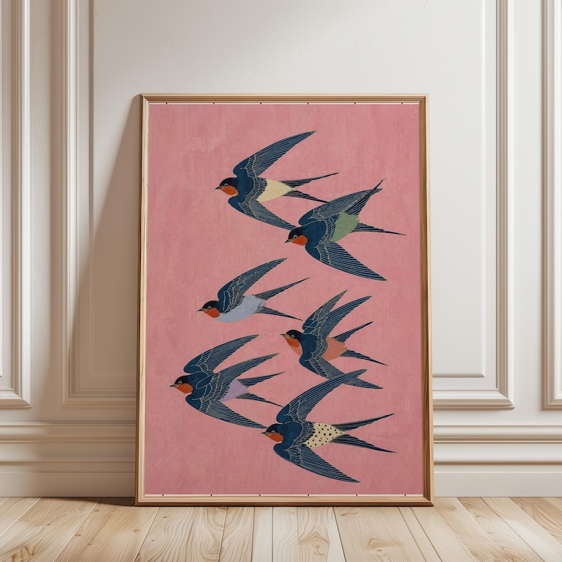Puede incluir: Una impresi&oacute;n art&iacute;stica enmarcada que representa una bandada de golondrinas en vuelo. Las aves tienen alas azul marino, gargantas rojas y detalles en amarillo, verde y blanco. El fondo es rosa suave y el marco es marr&oacute;n claro.