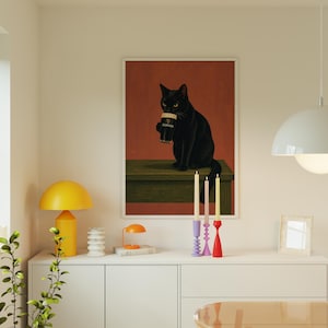 Puede incluir: Una impresi&oacute;n art&iacute;stica enmarcada representa un gato negro sosteniendo una pinta de Guinness. El gato est&aacute; sentado sobre una superficie verde contra un fondo rojo-naranja. La imagen est&aacute; enmarcada en blanco. La escena se complementa con candelabros coloridos.