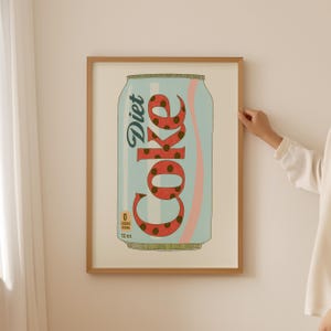 May include: A framed print of a Diet Coke can. The can is light blue with a pink stripe and the word "Diet Coke" in a stylized font. The "Coke" portion is red with brown polka dots. The can is labeled "0 calories" and "12 oz."