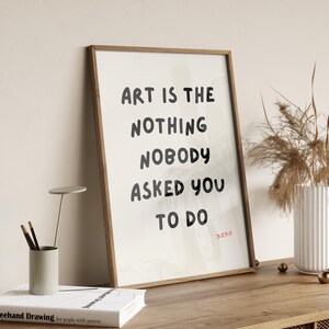 Op de afbeelding: Een ingelijst print met een witte achtergrond en zwarte tekst die "Art is the nothing nobody asked you to do" luidt, met het woord "Xoxo" in rood eronder.