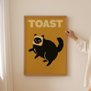 Può includere: Un poster incorniciato con un gatto nero con una fetta di pane tostato sulla testa, su uno sfondo giallo senape. La parola "TOAST" è stampata in grandi lettere beige in alto. Il poster è in una cornice di legno.