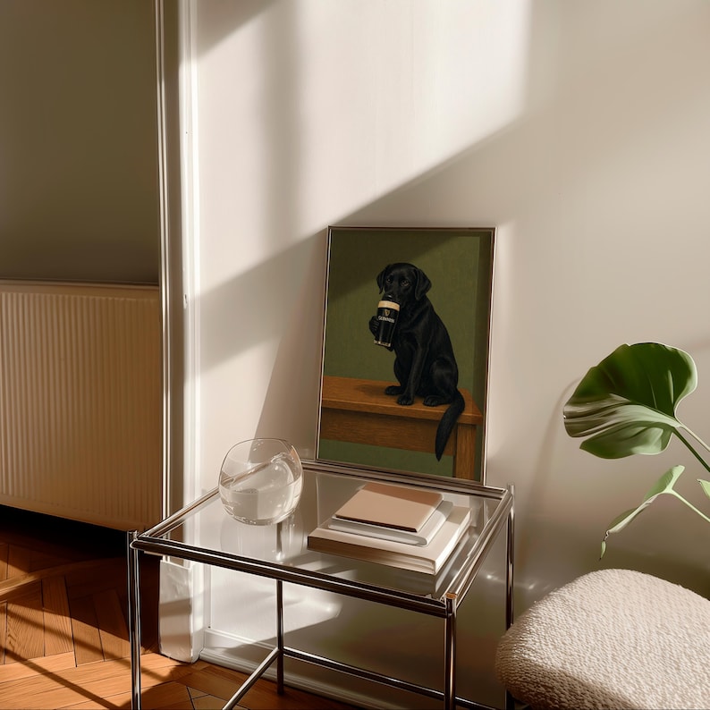 Pu&ograve; includere: Una stampa incorniciata con un Labrador Retriever nero che tiene in mano una pinta di stout. Il cane &egrave; seduto su una panca di legno su uno sfondo verde. La stampa &egrave; su un tavolo di vetro con libri e una ciotola di vetro trasparente.