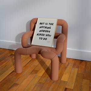 Op de afbeelding: Een ingelijst print met de tekst "Art is the nothing nobody asked you to do" op een lichtbruine stoel met een uniek ontwerp.