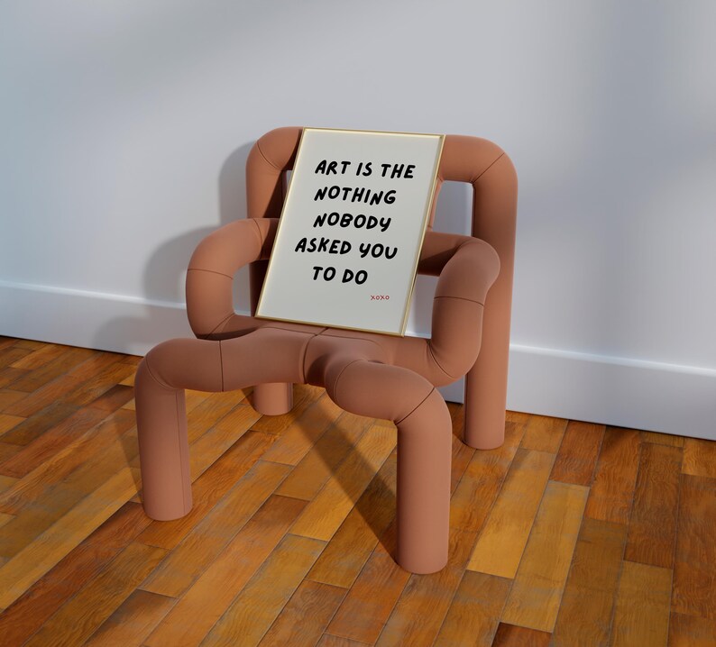 Op de afbeelding: Een ingelijst print met de tekst "Art is the nothing nobody asked you to do" op een lichtbruine stoel met een uniek ontwerp.