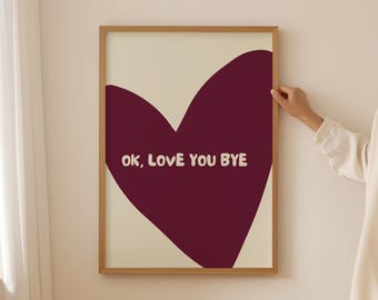 Könnte beinhalten: Ein gerahmter Kunstdruck mit einem großen weinroten Herz auf cremefarbenem Hintergrund. Die Worte "OK, LOVE YOU BYE" sind in Weiß über das Herz geschrieben. Der Rahmen ist hellbraun. Das Kunstwerk wird an einer Wand gezeigt.